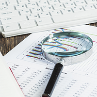 magnifying glass and documents with analytics data lying on table